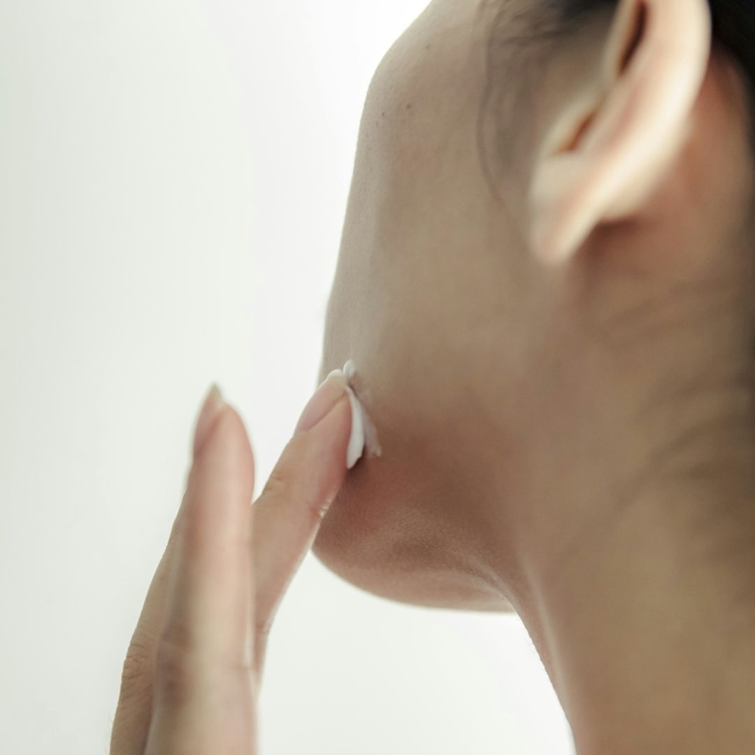 Closeup image of a white cream being applied to a woman's jawline