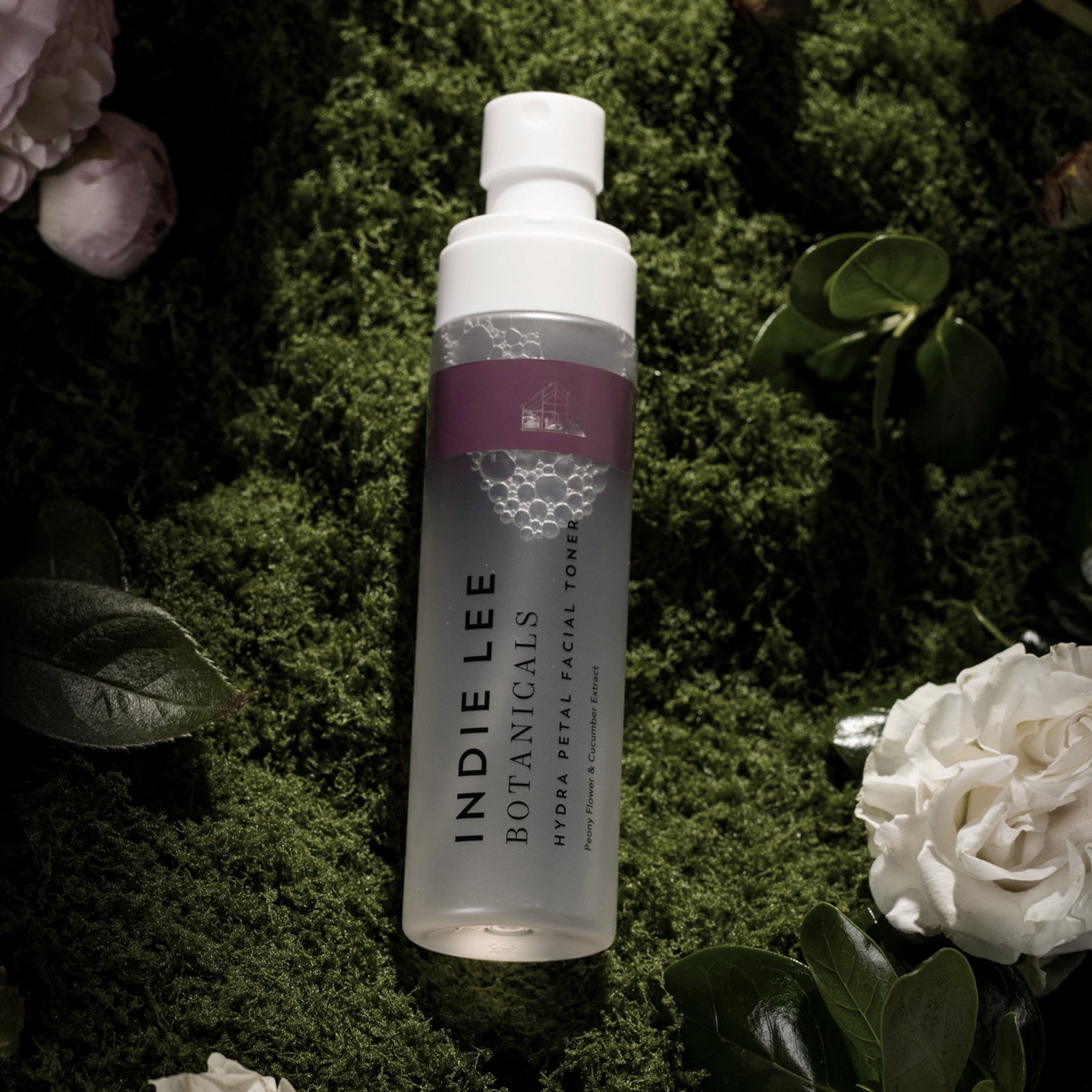 Indie Lee Botanicals facial toner bottle on a green leafy background with flowers.