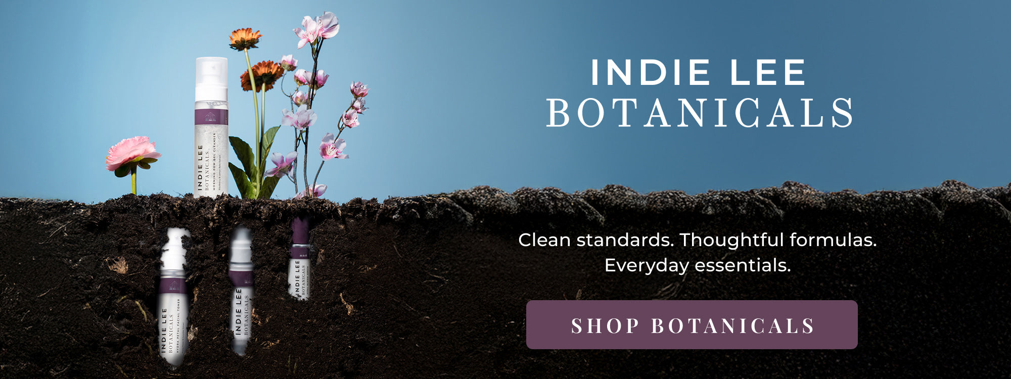 Indie Lee Botanicals products with flowers and soil on a blue background