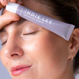 Woman holding a tube of Indie Lee Bronzing Drops next to her face