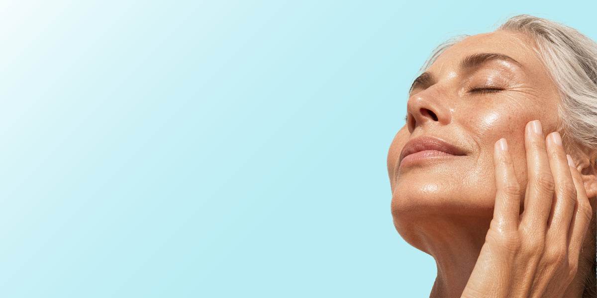 Close-up of a woman with closed eyes and her hand on her cheek, set against a solid light blue background.