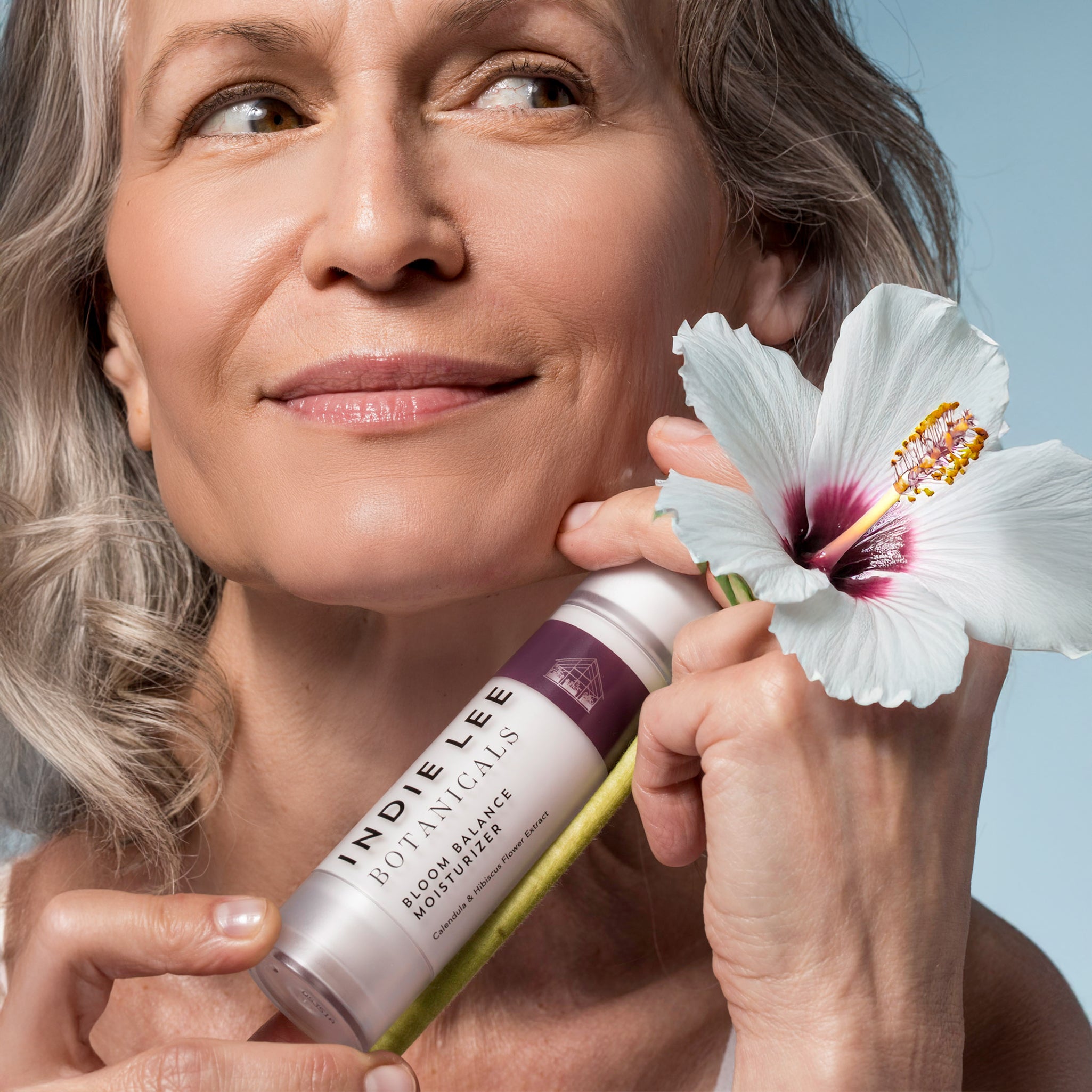Woman holding a bottle of Indie Lee Botanicals Bloom Balance Moisturizer with a flower in her hand