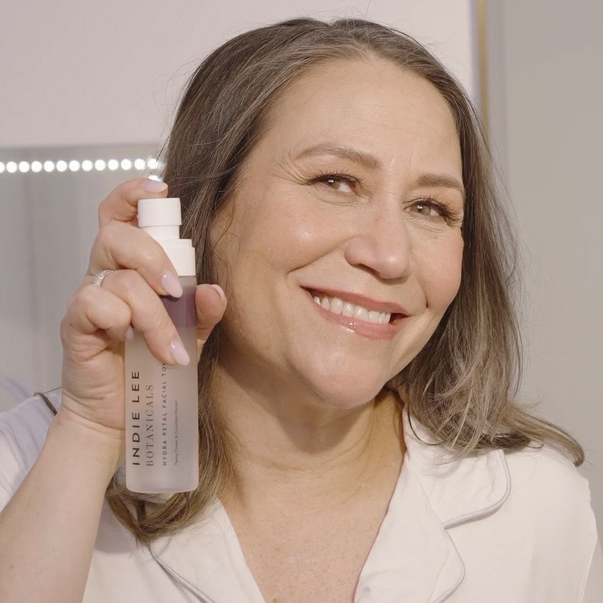 Indie Lee holding a bottle of Hydra Petal Facial Toner, smiling.