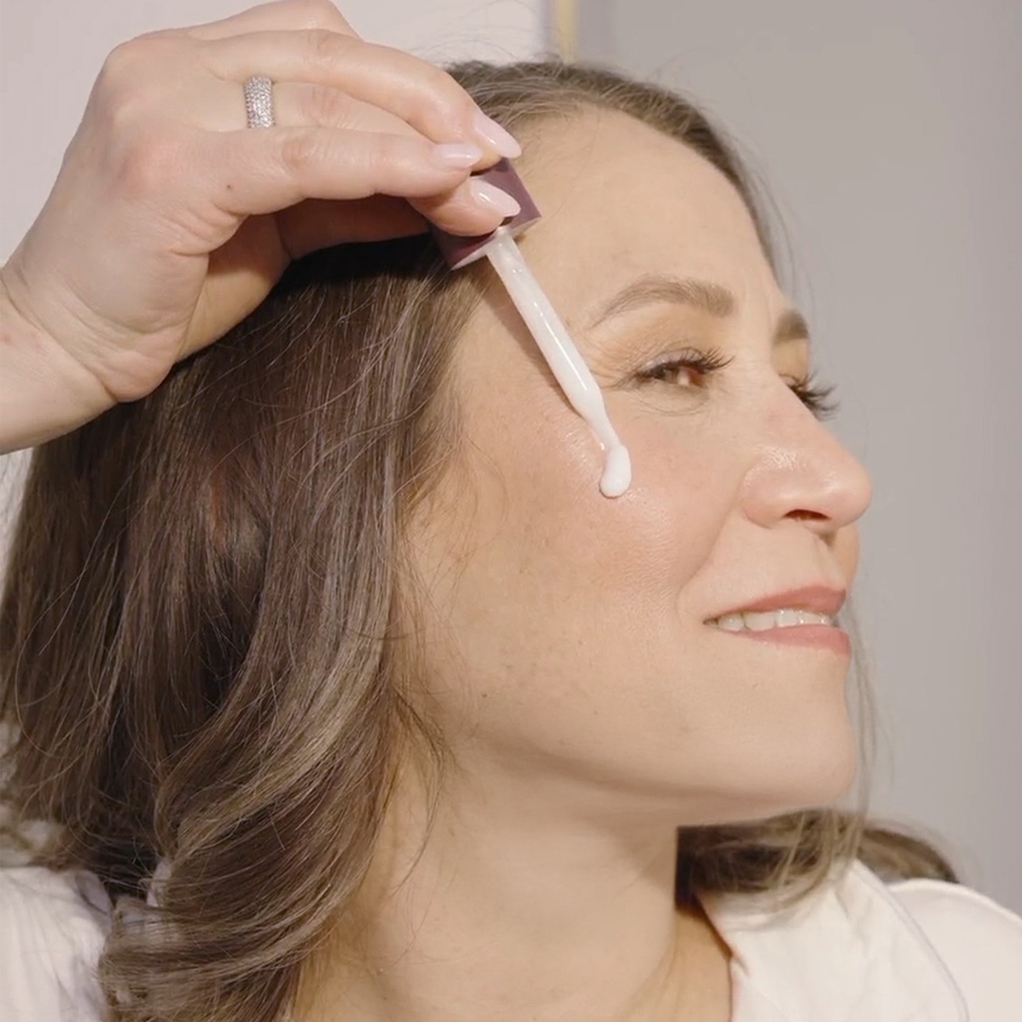 Indie Lee applying Vital Bloom Serum to her face using a dropper.