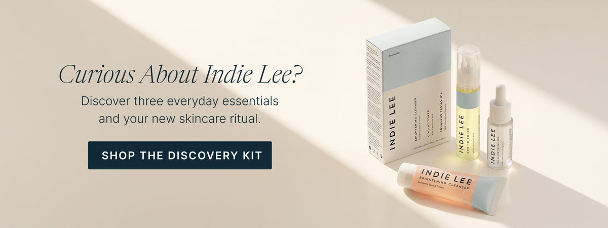 Indie Lee Discovery Kit featuring a white and light blue box, with travel sizes of Brightening Cleanser, COQ-10 Toner and Squalane Facial Oil on a beige background.