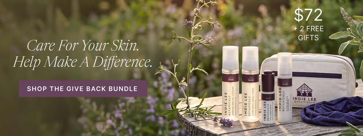 Indie Lee bundle including four bottles of skincare, a blue headband, and a makeup bag set on a wooden table against a natural background with promotional text 'Shop the give back bundle'