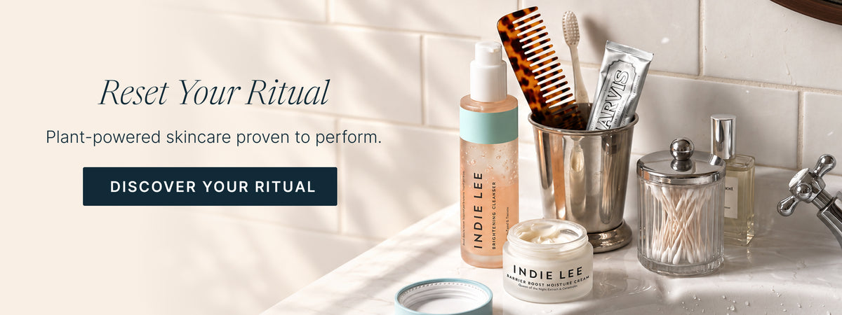 Assortment of Indie Lee skincare products arranged on a bathroom countertop with a white tile background and text 'Reset Your Ritual'
