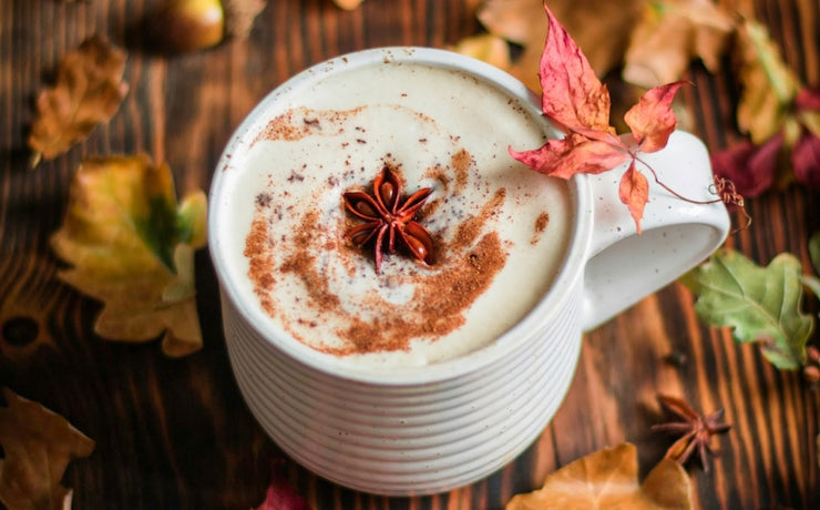A cozy fall scene featuring a mug of a warm beverage surrounded by autumn leaves