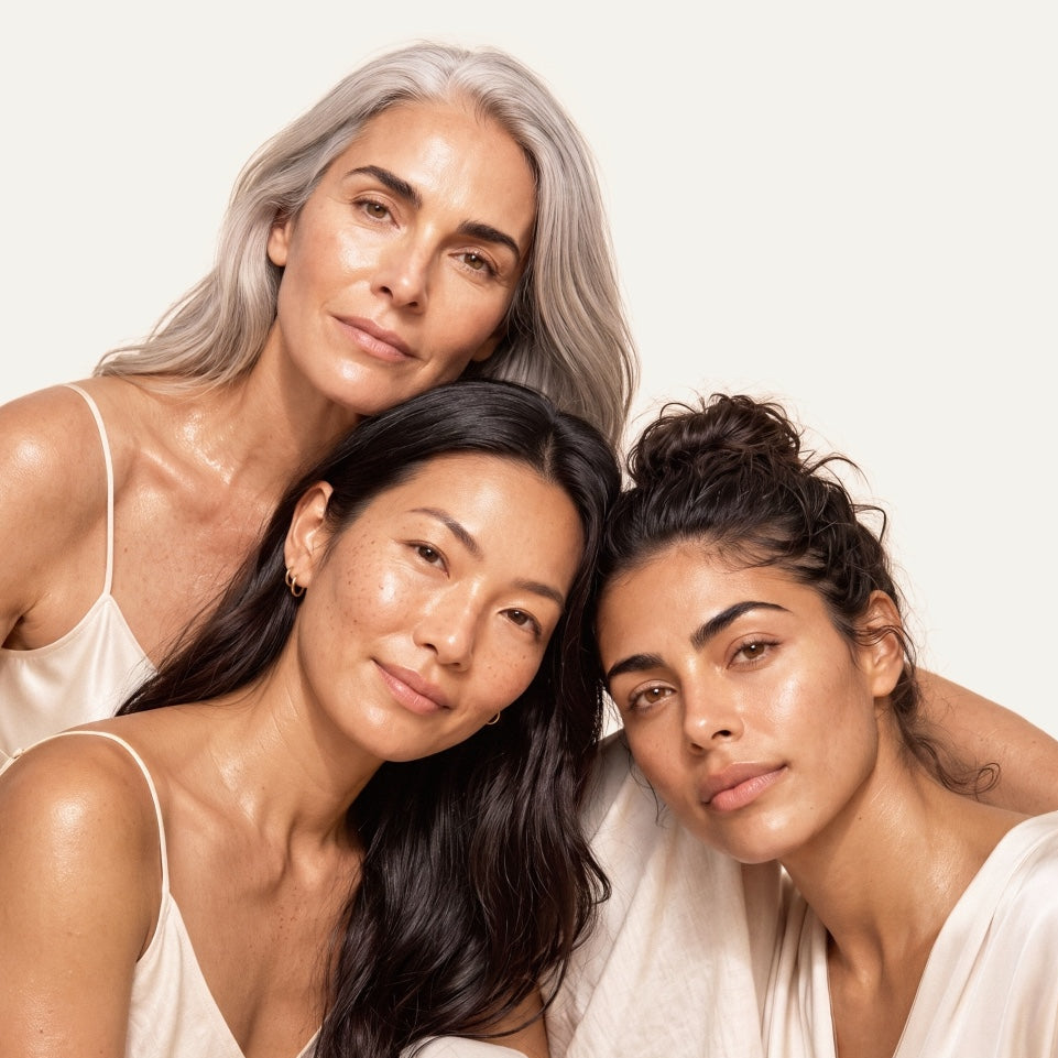 Three women with diverse hair colors and skin tones posing closely together against a solid off-white background.
