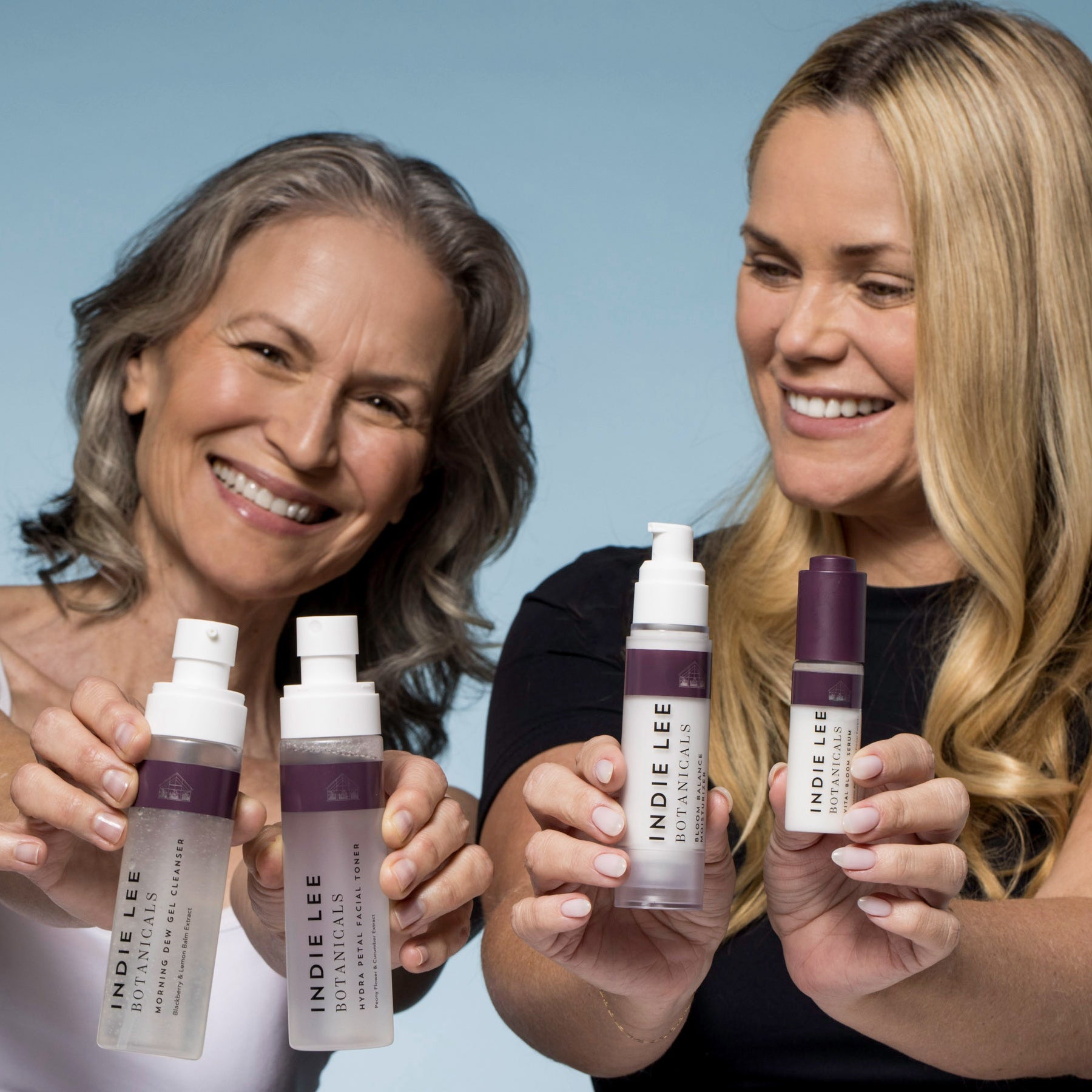 Two women holding bottles of Indie Lee products against a light blue background
