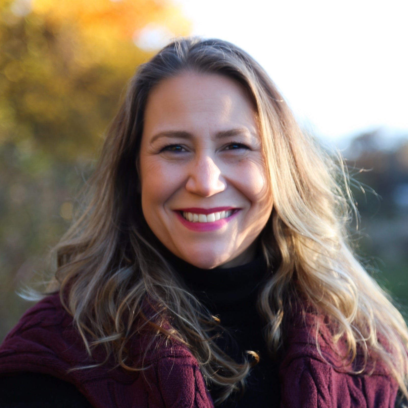 Indie Lee smiling outdoors with a blurred natural background